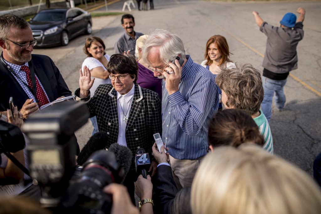 Sister Helen Prejean speaks to reporters outside the prison while Kim Van Atta, a friend of inmate Richard Glossip, talks to Glossip on the phone about his stay. In the background, Glossip's nephew celebrates the news. Photo by Shane Bevel/The Frontier